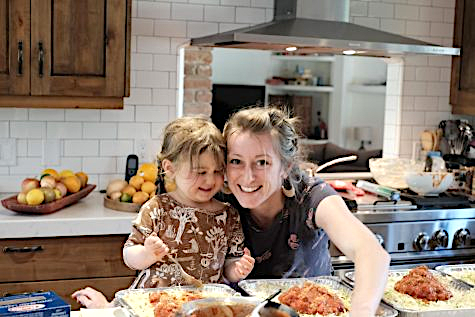 Lasagna Love founder Rhiannon Menn (right) leans in near her young daughter as they both spoon sauce into lasagna pans. The organization was founded through Menns desire to help families who were in need during the pandemic and has now expanded to anyone in a hardship. 