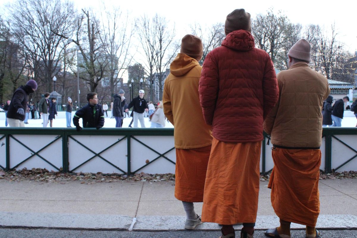 Three young men clad in orange robes watch on as families dance across the iced floor in the Boston common.