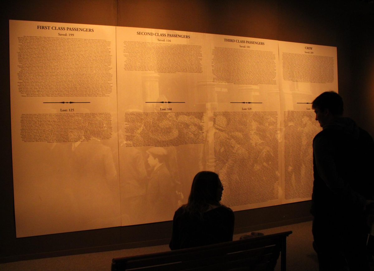 Museum goers look on at a wall listing the names of those who survived and perished in the Titanic tragedy.