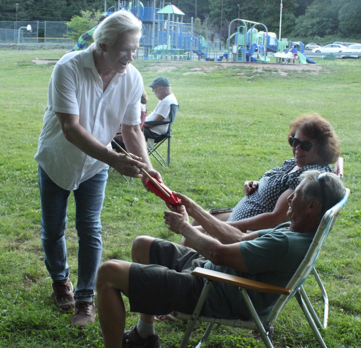 Center Line’s Johnny Russell hands an audience member a cowbell to play along with the band at Peterson Park in Wolcott, Conn., on June 29, 2025.